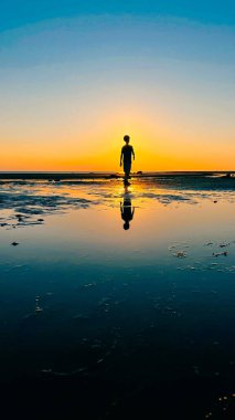 Çocuk gün batımında sahildeki deniz suyuna yansıdı. Yüksek kalite fotoğraf