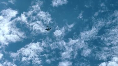 Açık mavi gökyüzünde uçan bir uçak. Dağılmış bulutlar, yer perspektifinden çekilmiş..