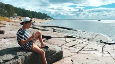 Bir insan güneşli bir gökyüzünün altında kayalık sahilde huzurlu ve huzurlu bir anın tadını çıkarıyor.