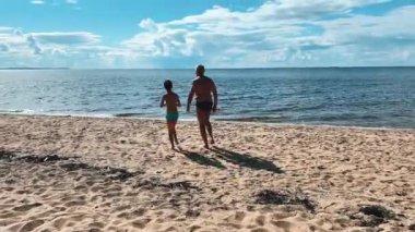 Kumsalda güzel, huzurlu bir gün. Bir anne ve çocuğu mutlu bir şekilde okyanus suyuna bakıyor.