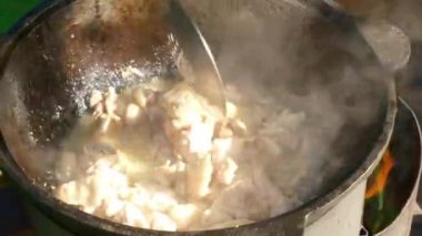 Tavuk büyük bir tencerede yavaşça karıştırılırken buhar dramatik bir şekilde yükselir ve inanılmaz derecede canlı bir yemek sahnesi yaratır.