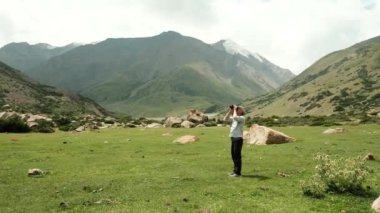 Uçsuz bucaksız yeşil bir arazide tek başına duran bir insan çarpıcı dağ manzarası ve manzarası ile çevrilidir.