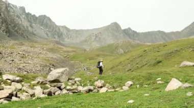 Yalnız bir yürüyüşçü kayalık arazi ve canlı yemyeşil ile süslenmiş huzurlu bir dağ vadisinde dikkatle gezinir.