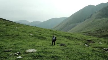 Yalnız bir yürüyüşçü, nefes kesen görkemli dağlarla çevrili yemyeşil tepeleri dikkatlice keşfeder.