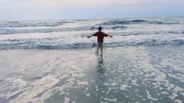 Neşeli ve kaygısız bir çocuk narin okyanus dalgalarında mutlu bir şekilde yürüyor, sahildeki hoş anları yakalıyor.