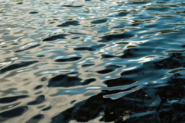 Dalgalanan suyun dinamik ve yüzeydeki ışığın güzel yansımalarını gösteren huzurlu bir görüntüsü.