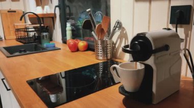 Sıcak ve rahat bir mutfak sahnesi, gösterişli bir Nespresso makinesi, parlak taze elmalar ve zarif mutfak aletleri.