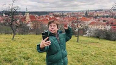 Neşeli bir çocuk heyecanlı bir şekilde Prag 'ın arka planında çarpıcı manzaralı bir selfie çekiyor.