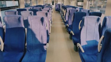 Doğal ışıkla aydınlatılmış, düzgün düzenlenmiş mavi koltuklar sergilenen davetkar ve ferah boş bir tren kompartımanı.