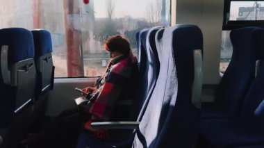 Sessiz ve sakin bir trenin iç kısmı bir yolcunun seyahat ederken akıllı telefon cihazına kendini kaptırdığını gösteriyor.