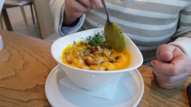 Bir el, taze otlar ve malzemelerle ustalıkla süslenmiş canlı bir çorba kasesinde parlak bir kaşık tutar.