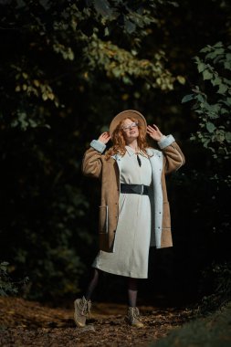 Sonbahar parkında poz veren şapkalı ve gözlüklü şık bir kız.