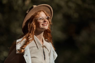 Sonbahar parkında poz veren şapkalı ve gözlüklü şık bir kız.