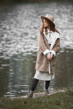 Parkta yürürken şapkalı güzel bir kadın ve gölde ceketli bir kadın..