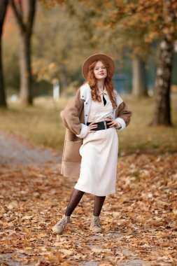 Beyaz önlüklü ve şapkalı güzel genç bir kadın parkta yürüyor. Sonbahar, sonbahar, mevsim ve moda. Sonbahar havası
