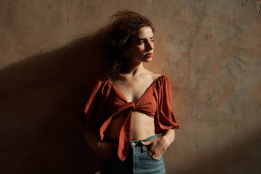 Stüdyoda poz veren kıvırcık saçlı ve kahverengi tişörtlü güzel bir kadın.