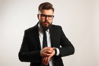 Genç işadamı elinde yay olan siyah bir takım elbise giyiyor, kameraya bakıyor ve beyaz bir arkaplanda düşünüyor.