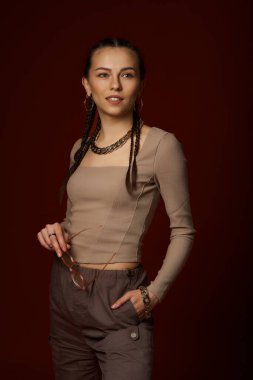 Kahverengi bluzlu güzel esmer kız portresi ve stüdyoda kahverengi arka planda zinciri olan siyah pantolon.