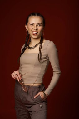 Kahverengi gömlekli, kırmızı pantolonlu ve kahverengi arka planda çapraz elli genç bir kadının portresi.