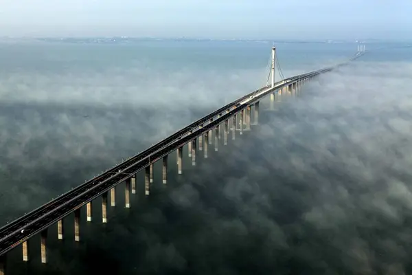 stock image aerial view of a long bridge emerging from dense fog over calm water