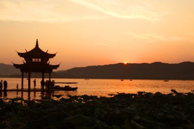 Hangzhou 'daki Batı Gölü' ndeki Lakeside Pavyonu 'nda günbatımının fotoğrafı.