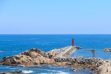 Kırmızı Deniz feneri, canlı mavi okyanusun kıyısındaki bir uçurumda.