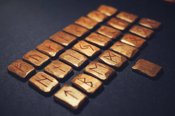 A stack of wooden runes. Wooden runes lie on a dark background. Runes are carved from wood, handmade. Each rune is marked with a symbol for divination. Elder Futhark rune set. Runes of Odin.