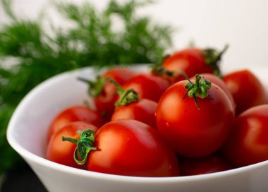 Dereotunun yanında beyaz bir tabakta küçük kırmızı domatesler, yan görüş, beyaz arkaplan