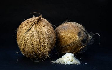 Two coconuts and the coconut shavings on the black background, space for text clipart