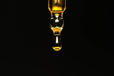 Siyah zemin üzerinde altın damlayan pipetin makro fotoğrafı, bakım ürünü.