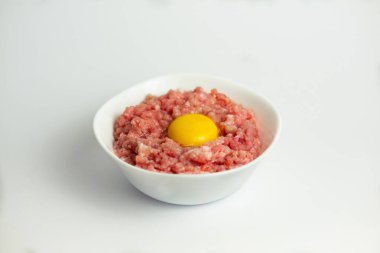 Beyaz arka planda, ortada çiğ yumurta bulunan doğranmış domuz eti (kıyma)..