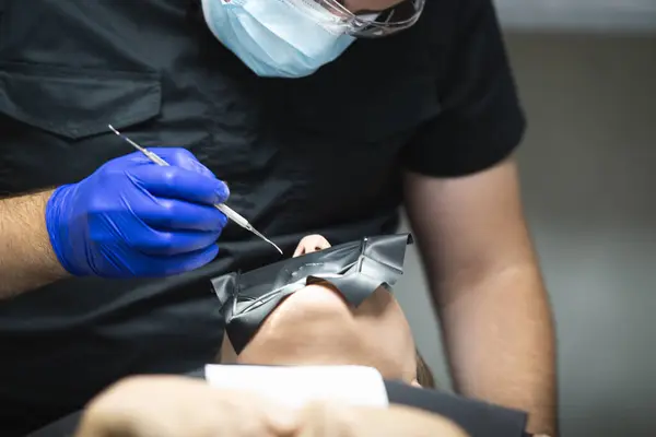 Bir doktor diş aletini tutar ve hastanın dişlerini tedavi eder..