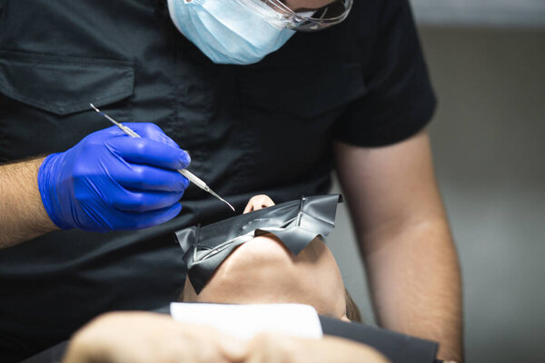 Врач держит в руках стоматологический инструмент и лечит зубы пациента.