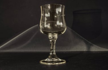 Siyah bir zemin üzerinde bir bardak şarap, arka planda kıvrımlı bir şekilde aydınlatıcı ışığı yansıtır.