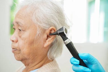 Audiologist use otoscope checking ear of elderly woman patient treating hearing loss problem.