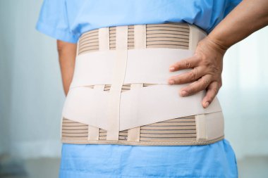 Ortopedik bel kemiği için sırt ağrısı destek kemeri takan Asyalı bir kadın hasta..