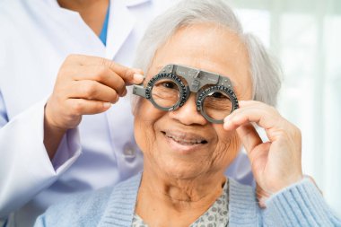 Optimetrist, Asyalı yaşlı kadın göz muayenesi yapıyor ve optik deneme çerçevesi kullanıyor.