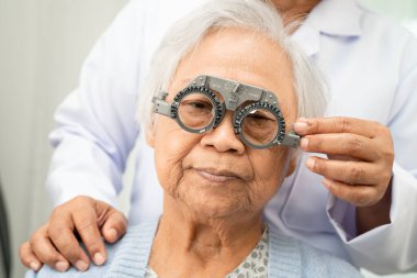 Optimetrist, Asyalı yaşlı kadın göz muayenesi yapıyor ve optik deneme çerçevesi kullanıyor.