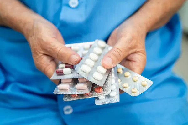 Üst düzey Asyalı kadın elinde kapsül hapları tutuyor. Tedavi için ambalajda ilaç var. Hastanedeki hasta enfeksiyon için..