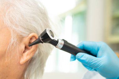 Audiologist use otoscope checking ear of elderly woman patient treating hearing loss problem.