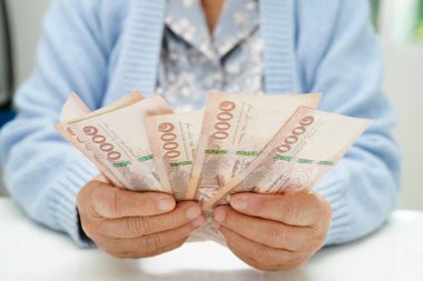 Emekli Asyalı yaşlı kadın para sayıyor ve aylık giderleri ve tedavi ücretini düşünüyor.