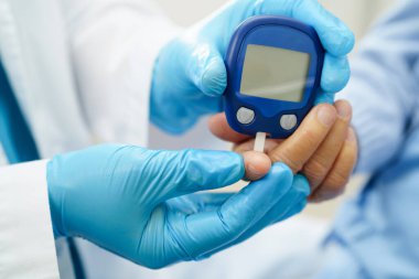 Diyabet tedavisinde kan şekeri seviyesini kontrol etmek için dijital glikoz ölçer kullanan Asyalı doktor.