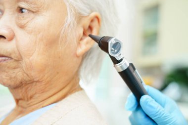 Otolaryngologist ya da ENT hekim doktoru yaşlı hasta kulağını otoskopla muayene ediyor, işitme sorunu var.. 