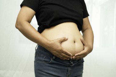 Şişman Asyalı kadın şişman göbeğini sıkmak için elini kullanıyor. Büyük boy aşırı kilolu ve obez..