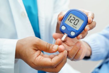 Diyabet tedavisinde kan şekeri seviyesini kontrol etmek için dijital glikoz ölçer kullanan Asyalı doktor.