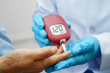 Diyabet tedavisinde kan şekeri seviyesini kontrol etmek için dijital glikoz ölçer kullanan Asyalı doktor.