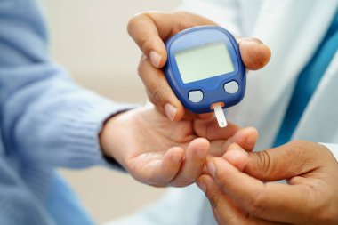 Diyabet tedavisinde kan şekeri seviyesini kontrol etmek için dijital glikoz ölçer kullanan Asyalı doktor.
