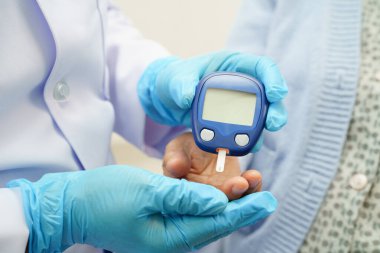 Diyabet tedavisinde kan şekeri seviyesini kontrol etmek için dijital glikoz ölçer kullanan Asyalı doktor.