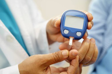 Diyabet tedavisinde kan şekeri seviyesini kontrol etmek için dijital glikoz ölçer kullanan Asyalı doktor.
