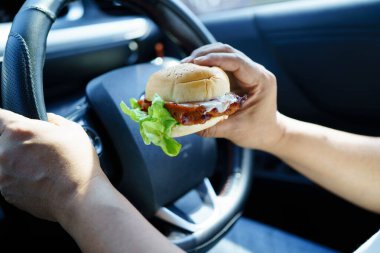 Asyalı kadın sürücü arabada hamburger yiyerek bekliyor..